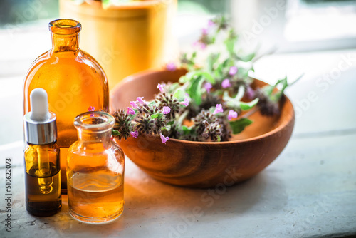 Apothecary bottles near raw materials from fresh flowering Clinopodium vulgare, Wild basil, rhizomatous perennial herb collected in ecologically clean region of Ukraine. Cosmetics from medicinal herbs photo