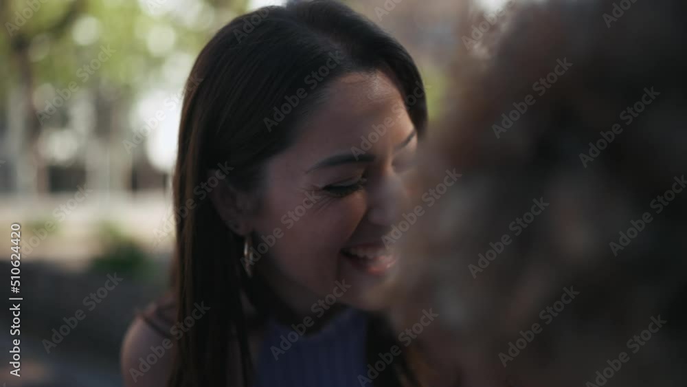 Cheerful brunette woman talking with her girlfriend while sitting on the bench outdoors Cheerful brunette woman talking with her girlfriend while sitting on the bench outdoors