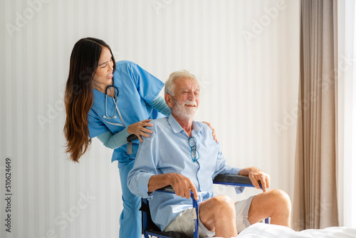 Friendly staff caregiver of nursing home talking to elderly man on wheelchair in the bedroom. © kelvn