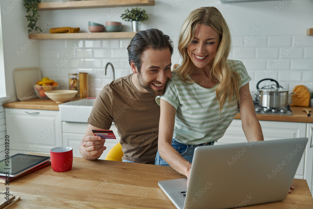 Happy young couple using credit card while shopping online from home Happy young couple using credit card while shopping online from home