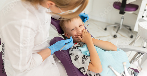Little cute boy in the dentist's chair in the office is afraid to treat his teeth