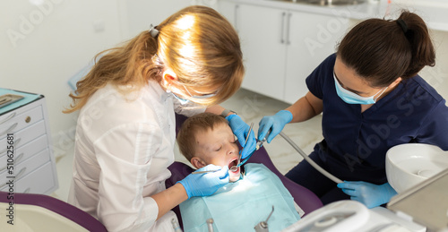 Dentist and assistant examining kid mouth with dentistry equipment instrument. Teeth treatment for children. Stomatology and orthodontology