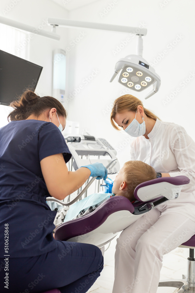 Dentist and assistant examining kid mouth with dentistry equipment instrument. Teeth treatment for children. Stomatology and orthodontology Dentist and assistant examining kid mouth with dentistry equipment instrument. Teeth treatment for children. Stomatology and orthodontology