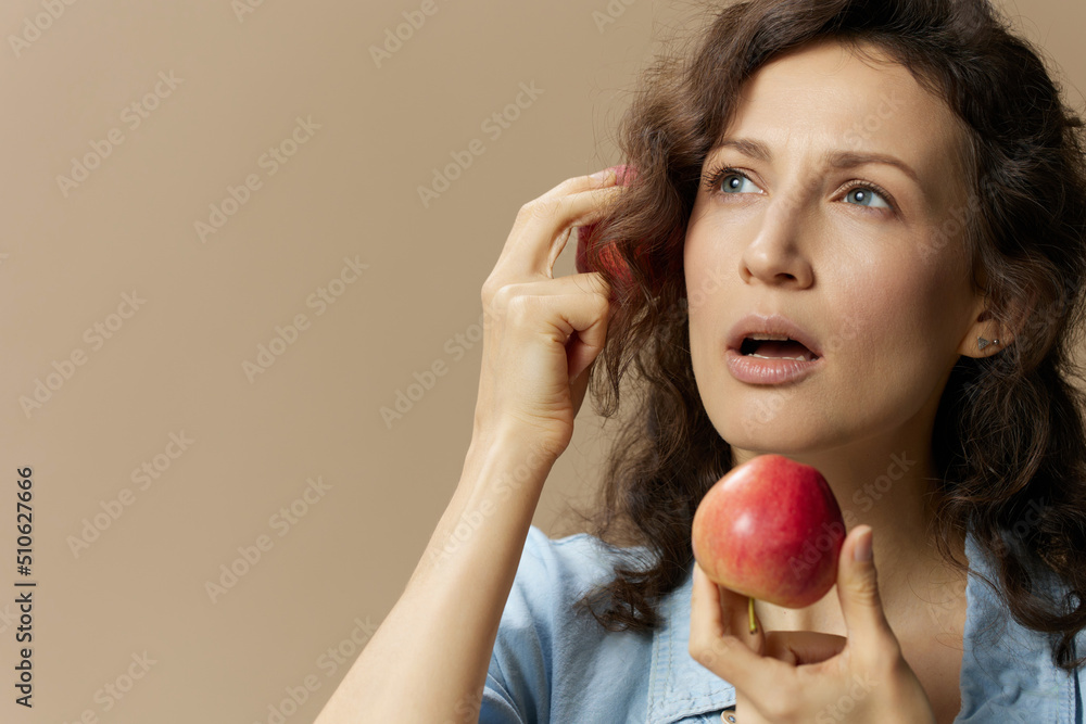Funny focused curly beautiful lady in jeans casual shirt holds apples as walkie-talkie posing isolated on over beige pastel background. Healthy food. Natural eco-friendly products concept. Copy space Funny focused curly beautiful lady in jeans casual shirt holds apples as walkie-talkie posing isolated on over beige pastel background. Healthy food. Natural eco-friendly products concept. Copy space