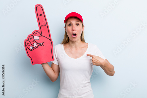 blonde young adult woman looking shocked and surprised with mouth wide open, pointing to self. number one fan concept photo