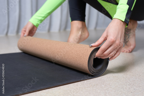 Image of a young woman in a gymnastics suit rolling up a mat after a workout. The concept of fitness  yoga  pilates.