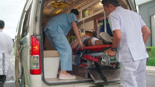 Staff man and emergency team bring patient lie on stretcher bed into ambulance van and other staff help to support the patient.