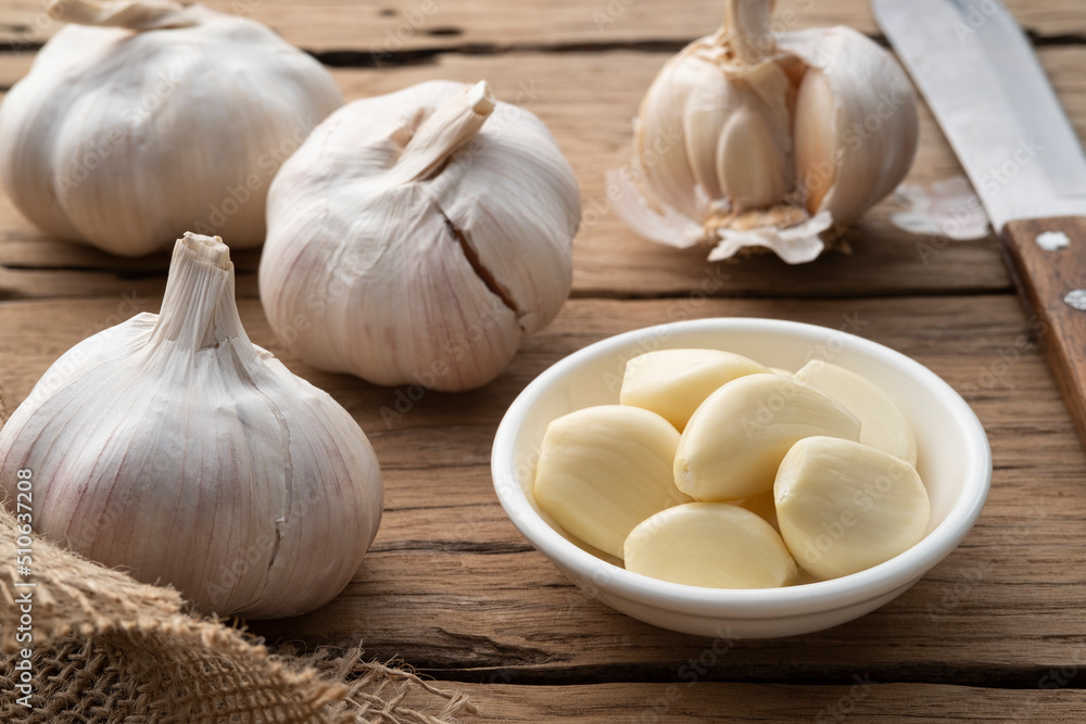 Peeled garlic in a bowl and garlic cloves on the wooden plate Peeled garlic in a bowl and garlic cloves on the wooden plate
