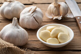 Peeled garlic in a bowl and garlic cloves on the wooden plate