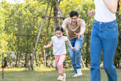 Asian girl running on the lawn in a public garden Do activities together with your family in a fun and joyful way. There is a father and mother taking care of them closely. © SKW