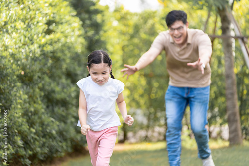 Asian girl running on the lawn in a public garden Do activities together with your family in a fun and joyful way. There is a father and mother taking care of them closely. © SKW