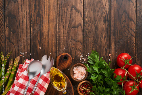 Parsley, parsley, tomato, garlic, olive oil, pepper, salt and salad fork and spoon on wooden cooking background. Food cooking background. Ingredients for cooking food background. Mock up. Top view.