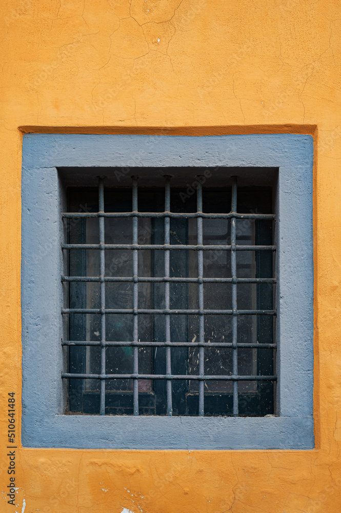 An old small window with a square lattice, like a prison on the yellow wall