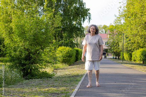Obraz na plátne An elderly woman in shorts with gray hair walks through the park