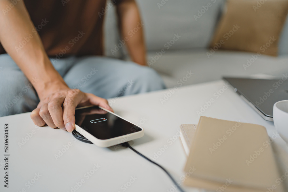 Fototapeta premium Man hands plugging a charger in a smart phone. Charging Smartphone with Wireless Charging Pad at Home