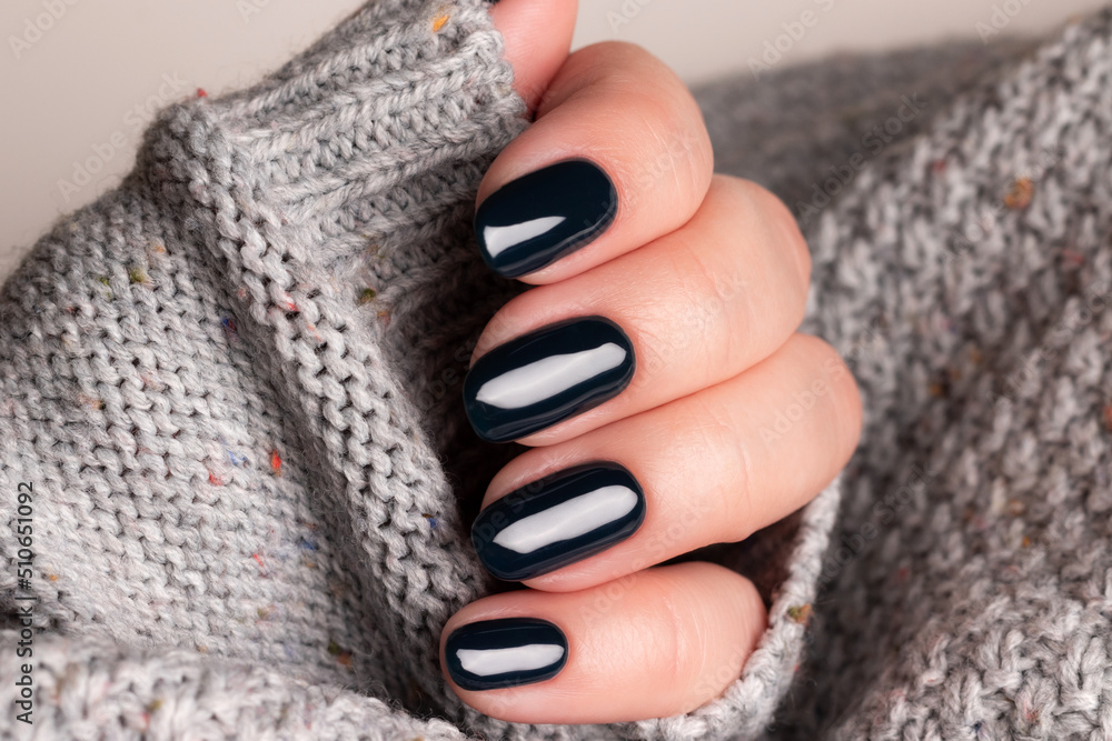 Φωτογραφία Female hand in gray knitted sweater with beautiful manicure - dark black nails