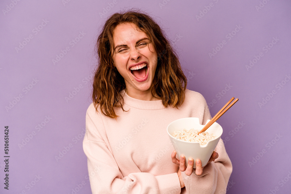 Young caucasian woman eating noodles isolated on purple background laughing and having fun. Young caucasian woman eating noodles isolated on purple background laughing and having fun.