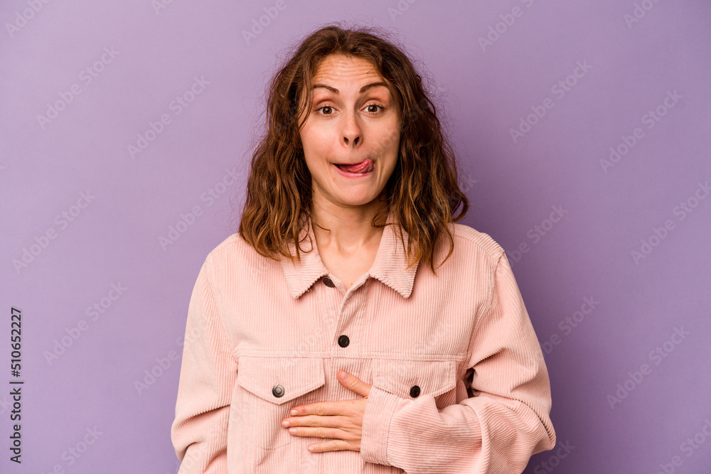 Young caucasian woman isolated on purple background touches tummy, smiles gently, eating and satisfaction concept. Young caucasian woman isolated on purple background touches tummy, smiles gently, eating and satisfaction concept.
