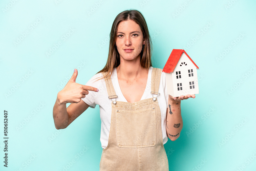 Young caucasian pregnant woman holding an toy house isolated on blue background person pointing by hand to a shirt copy space, proud and confident Young caucasian pregnant woman holding an toy house isolated on blue background person pointing by hand to a shirt copy space, proud and confident