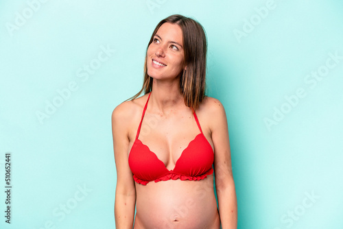 Young caucasian pregnant woman wearing bikini isolated on blue background dreaming of achieving goals and purposes © Asier