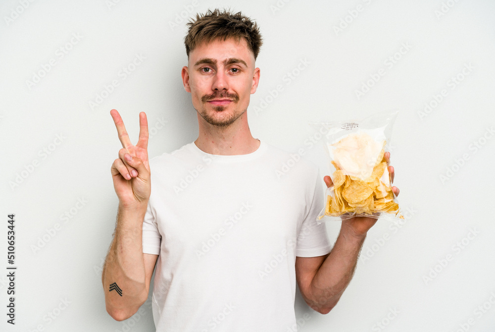 Young caucasian man holding crisps isolated on white background showing number two with fingers. Young caucasian man holding crisps isolated on white background showing number two with fingers.