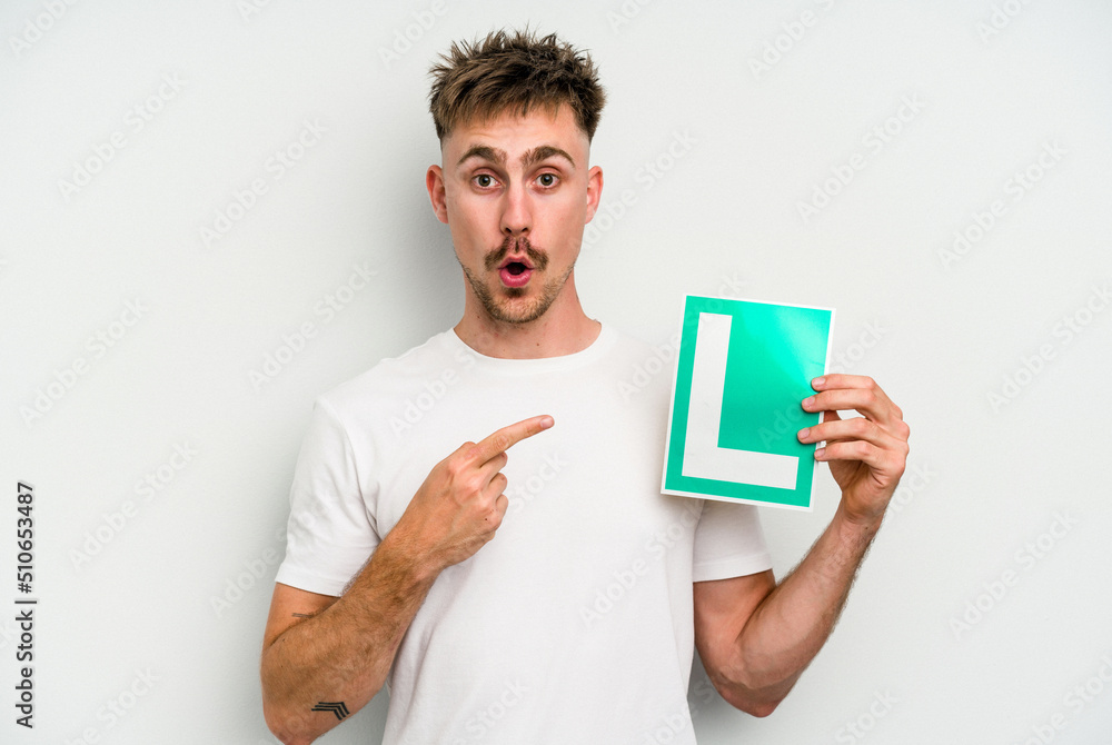 Young caucasian man holding L placard isolated on white background pointing to the side Young caucasian man holding L placard isolated on white background pointing to the side