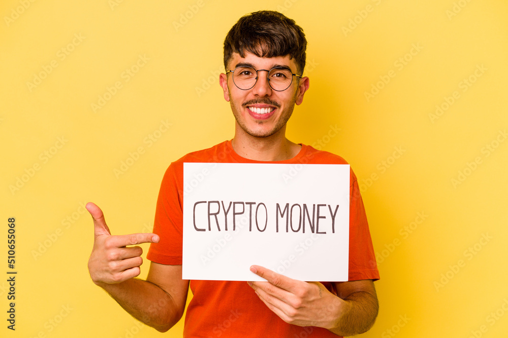 Young hispanic man holding nft placard isolated on yellow background person pointing by hand to a shirt copy space, proud and confident Young hispanic man holding nft placard isolated on yellow background person pointing by hand to a shirt copy space, proud and confident