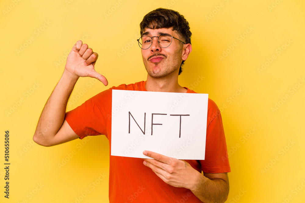 Young hispanic man holding nft placard isolated on yellow background feels proud and self confident, example to follow. Young hispanic man holding nft placard isolated on yellow background feels proud and self confident, example to follow.