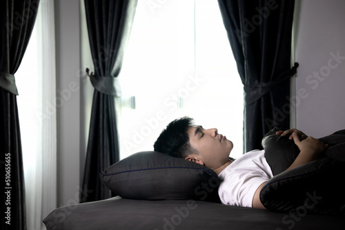Side view of an Asian man lying in bed with a bright face in the morning. Health care concept with at least eight hours of sleep