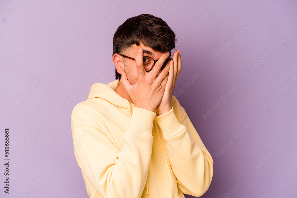 Young caucasian man isolated on purple background blink through fingers frightened and nervous. Young caucasian man isolated on purple background blink through fingers frightened and nervous.