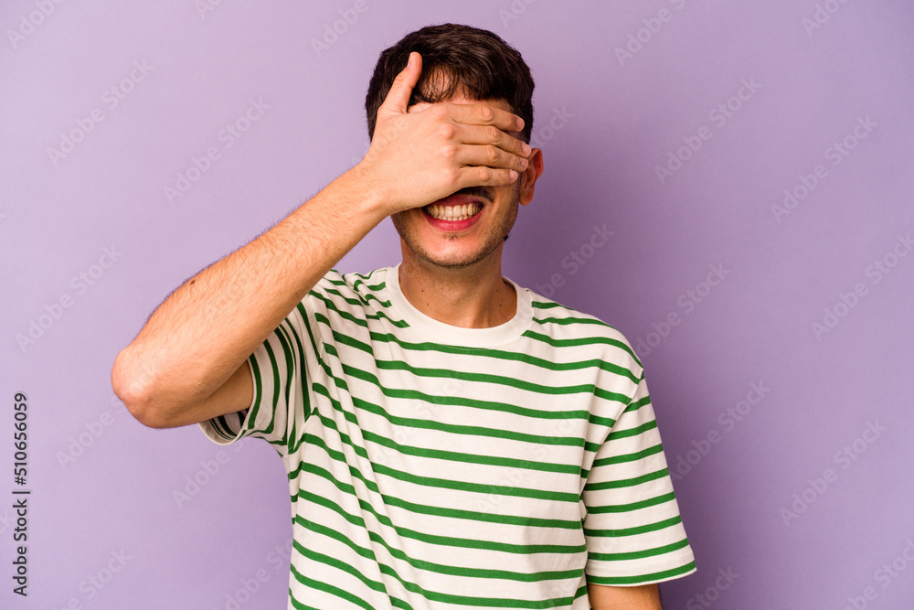 Young caucasian man isolated on purple background covers eyes with hands, smiles broadly waiting for a surprise. Young caucasian man isolated on purple background covers eyes with hands, smiles broadly waiting for a surprise.