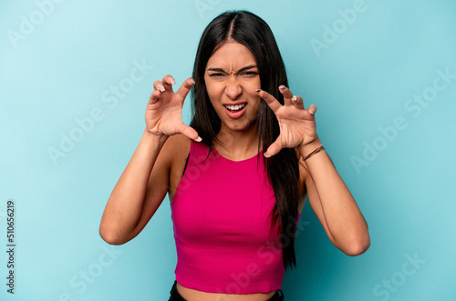 Young hispanic woman isolated on blue background showing claws imitating a cat, aggressive gesture. © Asier