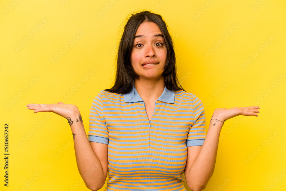 Young hispanic woman isolated on yellow background confused and doubtful shrugging shoulders to hold a copy space. Young hispanic woman isolated on yellow background confused and doubtful shrugging shoulders to hold a copy space.
