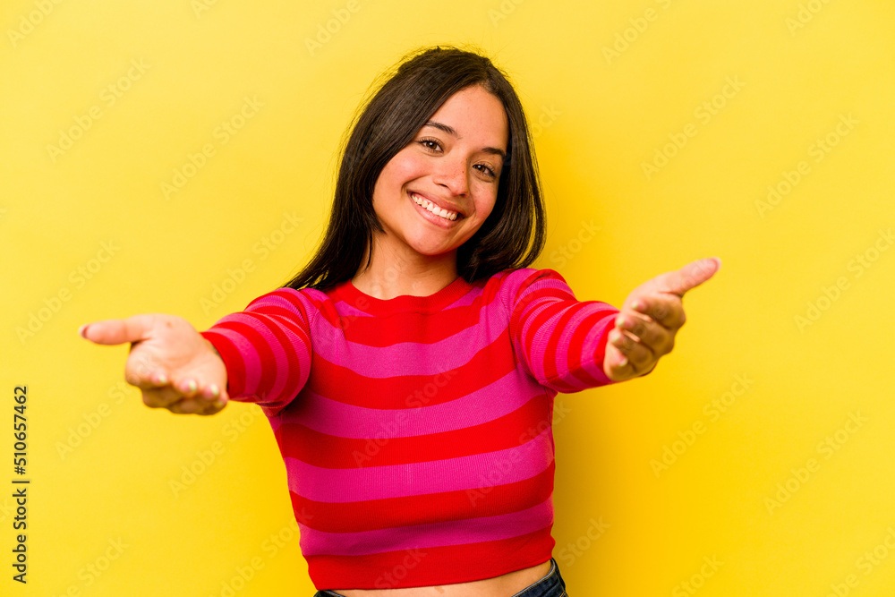 Young hispanic woman isolated on yellow background showing a welcome expression.