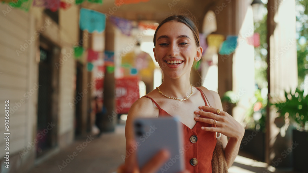 Сlose-up young woman takes a selfie, video call on the street on urban background. Smiling girl use social media, streaming service