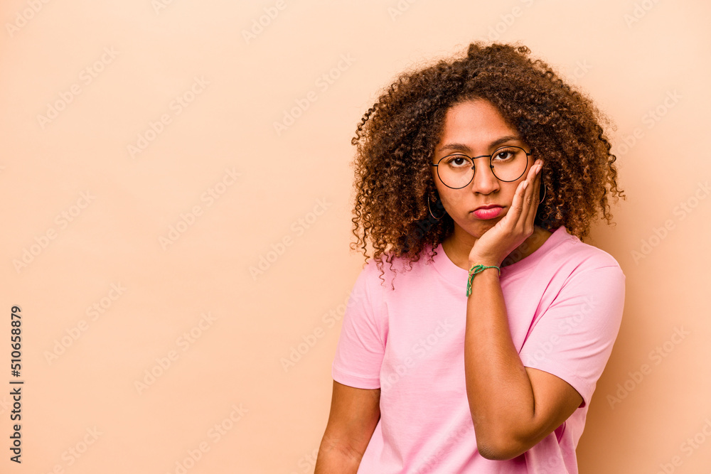 Young African American woman isolated on beige background who feels sad and pensive, looking at copy space. Young African American woman isolated on beige background who feels sad and pensive, looking at copy space.