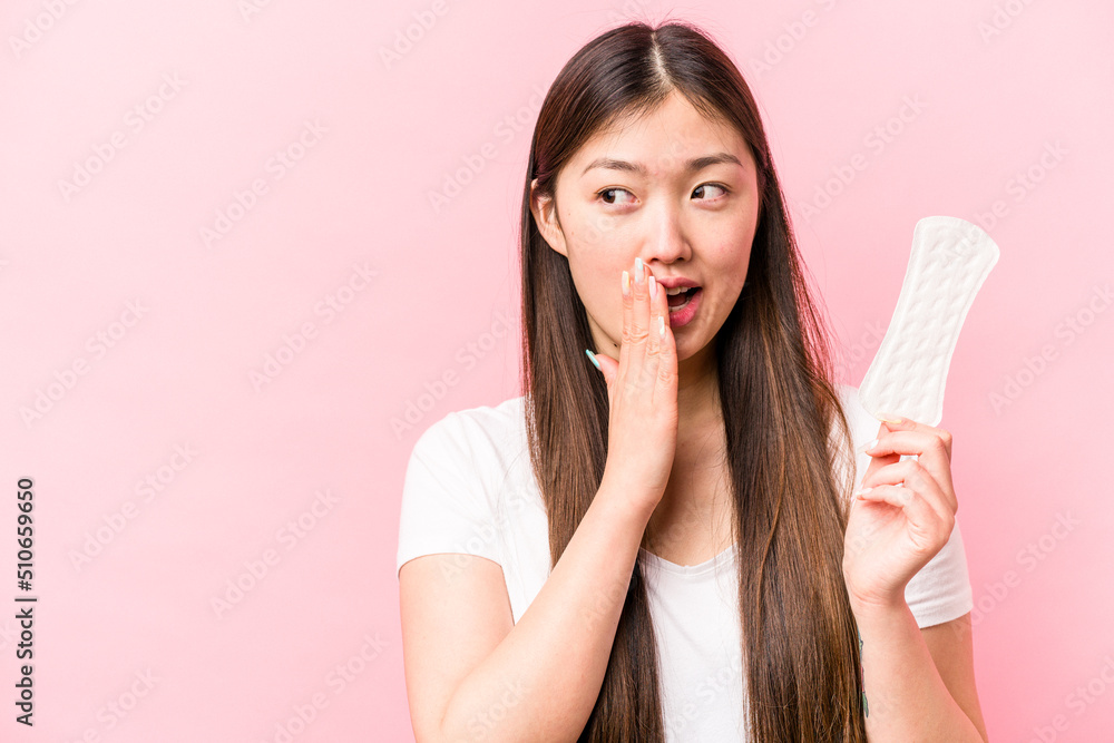 Young asian woman holding sanitary napkin isolated on pink background is saying a secret hot braking news and looking aside Young asian woman holding sanitary napkin isolated on pink background is saying a secret hot braking news and looking aside