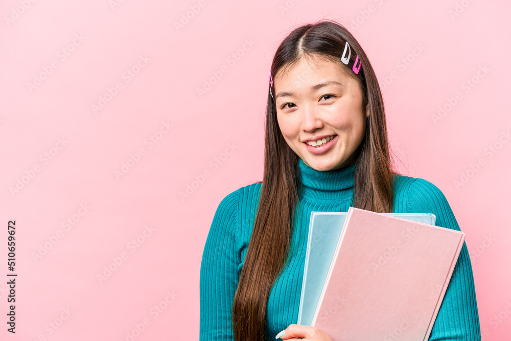 Young asian student woman holding books isolated on pink background happy, smiling and cheerful. Young asian student woman holding books isolated on pink background happy, smiling and cheerful.