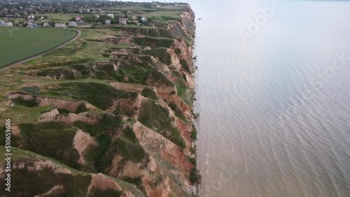 Quadcopter flies over hills and a wide river, approaching a village with yards