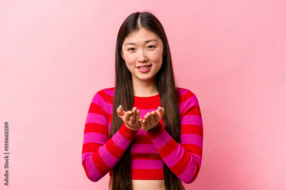 Young Chinese woman isolated on pink background holding something with palms, offering to camera. Young Chinese woman isolated on pink background holding something with palms, offering to camera.