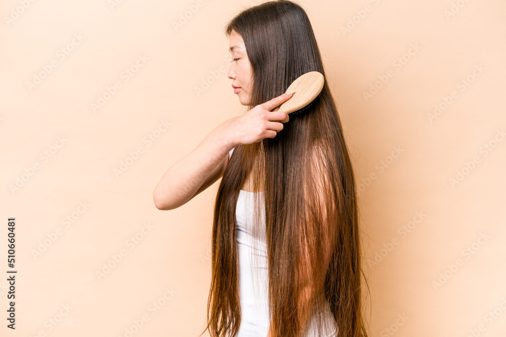 Young asian woman combing her hair isolated on beige background Young asian woman combing her hair isolated on beige background