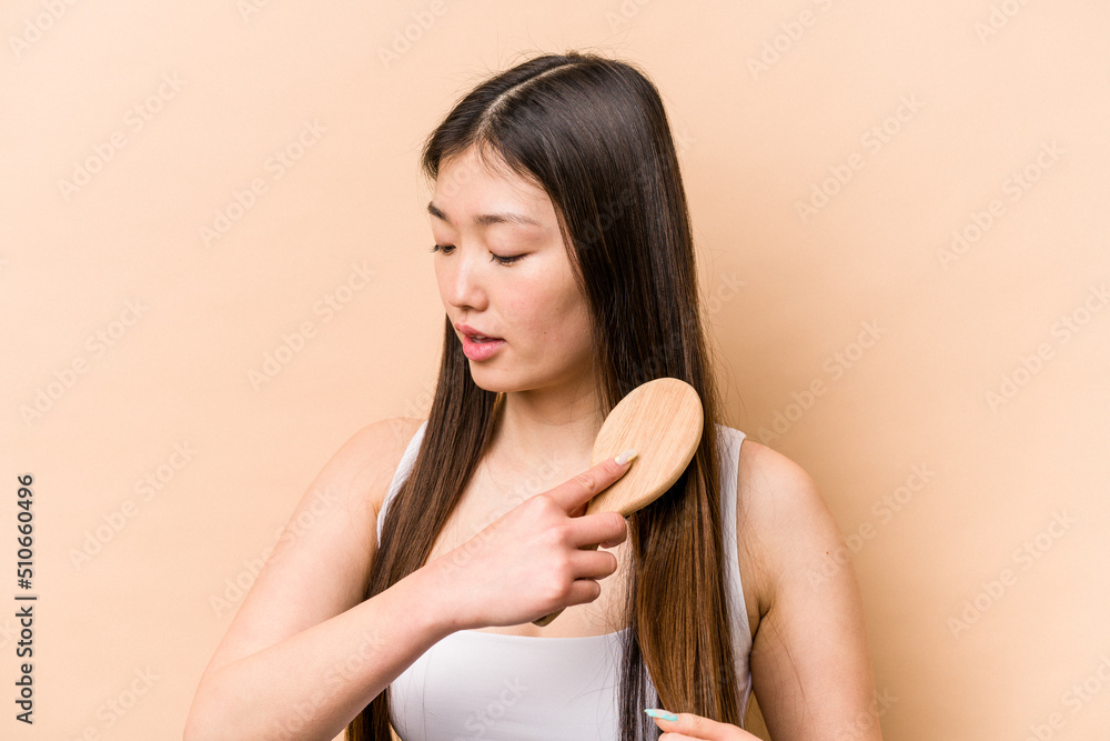 Naklejka premium Young asian woman combing her hair isolated on beige background