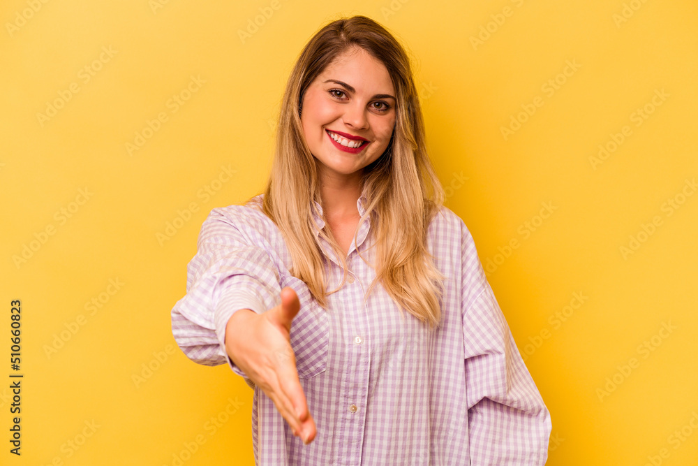 Young caucasian woman isolated on yellow background stretching hand at camera in greeting gesture. Young caucasian woman isolated on yellow background stretching hand at camera in greeting gesture.