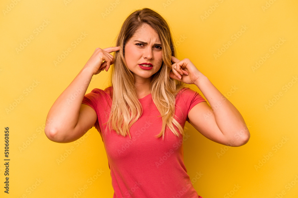 Young caucasian woman isolated on yellow background covering ears with fingers, stressed and desperate by a loudly ambient. Young caucasian woman isolated on yellow background covering ears with fingers, stressed and desperate by a loudly ambient.