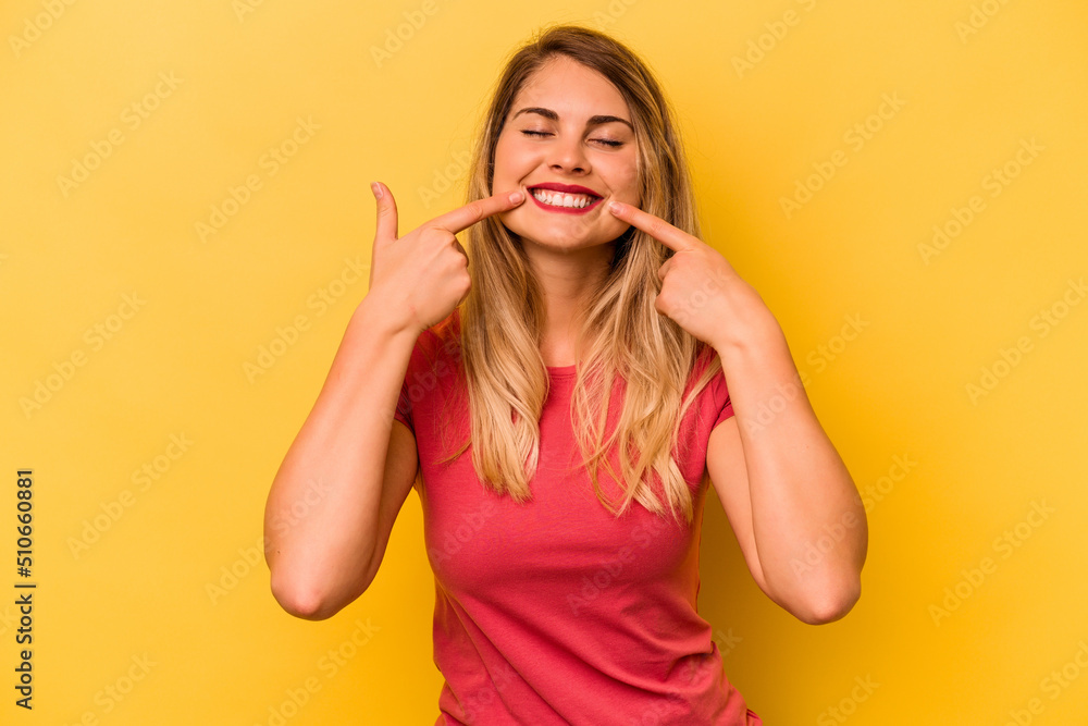 Young caucasian woman isolated on yellow background smiles, pointing fingers at mouth. Young caucasian woman isolated on yellow background smiles, pointing fingers at mouth.