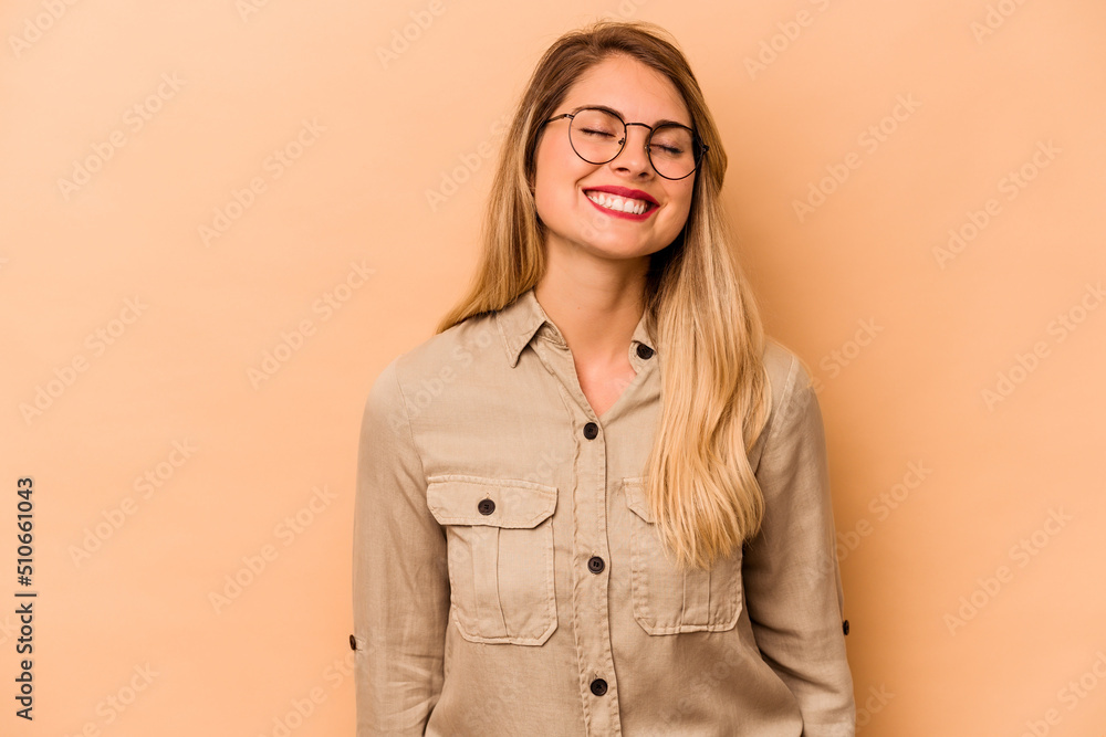 Young caucasian woman isolated on beige background laughs and closes eyes, feels relaxed and happy.