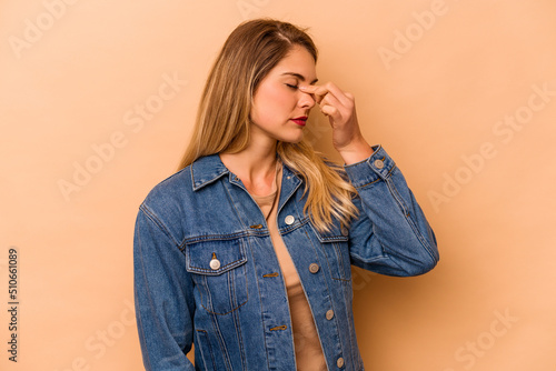 Young caucasian woman isolated on beige background having a head ache, touching front of the face.