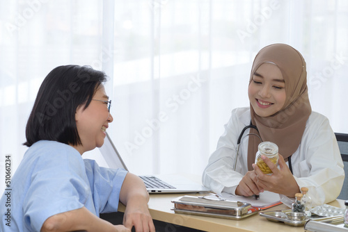 Young asian woman muslim doctor holding the bottle of pills and explaining to elderly patient in the hospital office