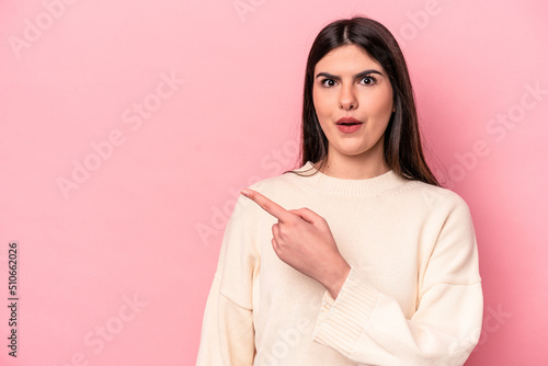 Young caucasian woman isolated on pink background pointing to the side © Asier