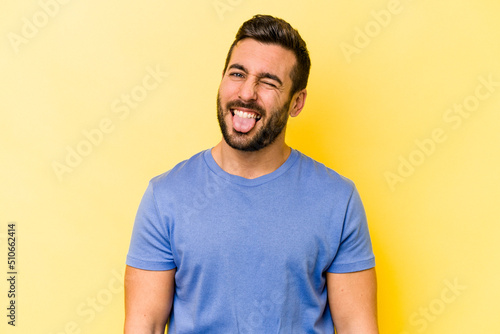 Young caucasian man isolated on yellow background funny and friendly sticking out tongue.